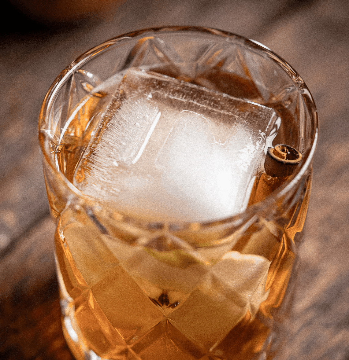 Apple Crisp cocktail in a rocks glass over one large clear cube, garnished with a thin apple slice and a charred cinnamon stick.