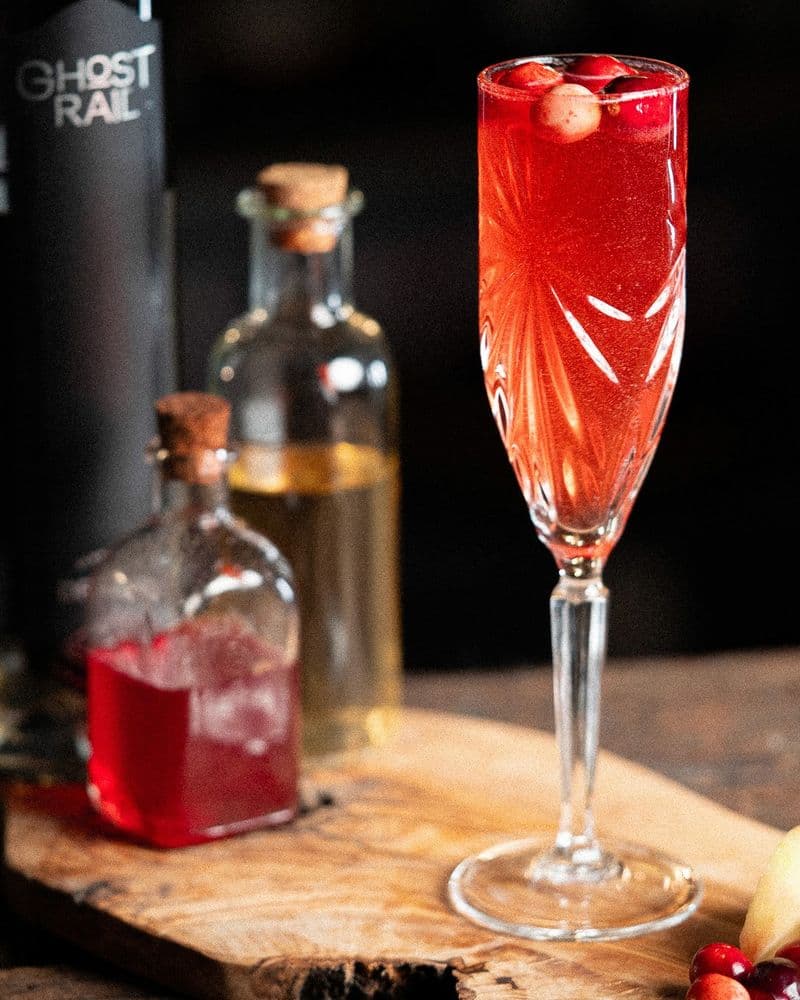 Hard cidre being poured slowly into the Autumn 75, the gin-cranberry base catching the light.