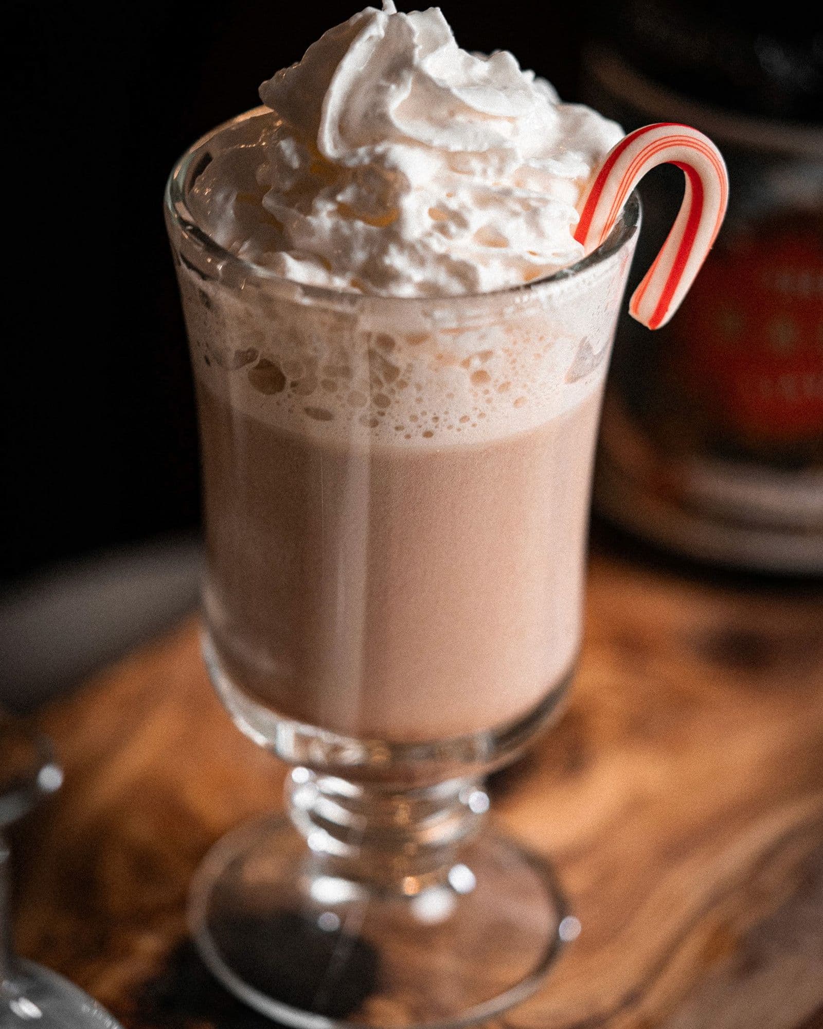 Candy Cane Cocoa in a chilled coupe topped with whipped cream and a mini candy cane.