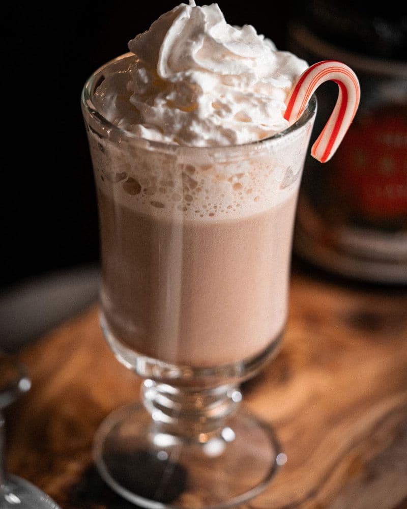 Candy Cane Cocoa in a chilled coupe topped with whipped cream and a mini candy cane.