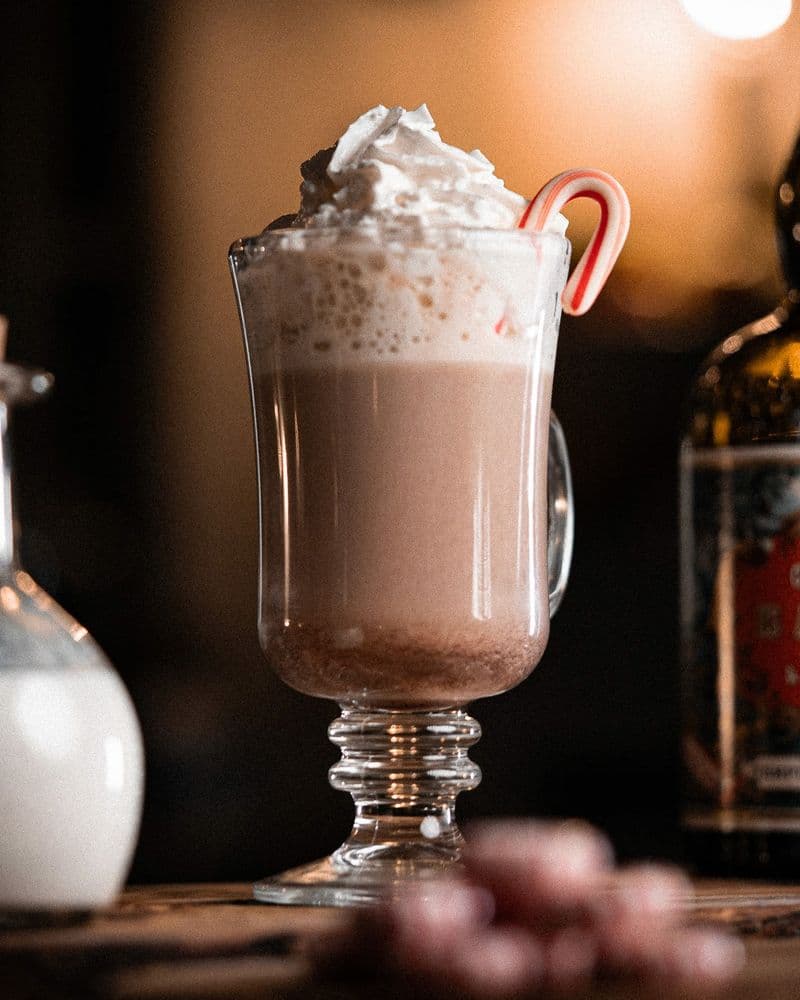 Candy Cane Cocoa staged on a wooden tray with peppermint, cocoa powder, and a candy cane.