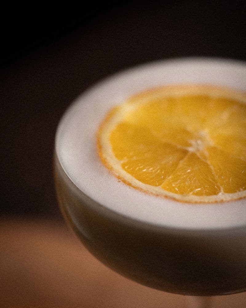 Fresh oranges and a Gift of Gold cocktail set together against a warm-dark background.