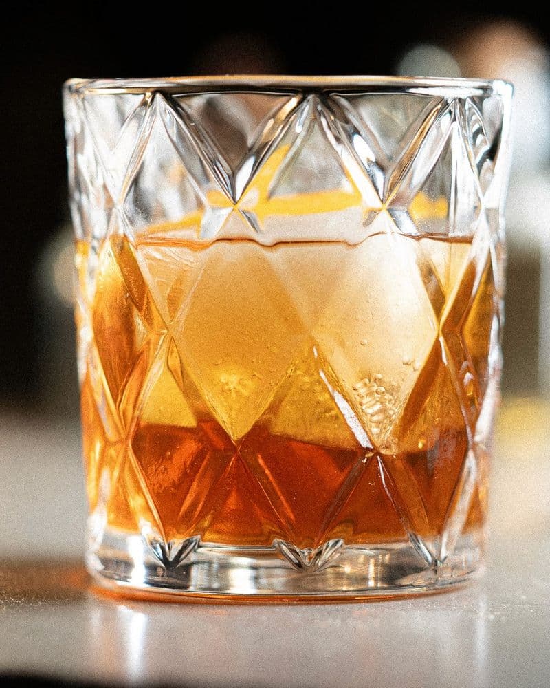 Old-Fashioned Christmas on a candlelit bar with pecan halves and an orange beside the glass.